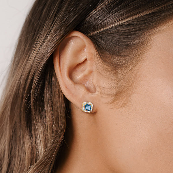 Woman wearing blue and gold square halo stud earrings