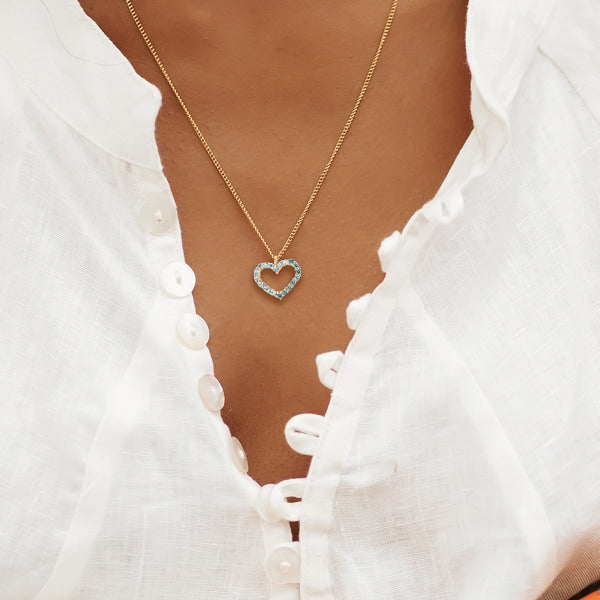 Woman wearing a blue crystal open heart on a gold necklace