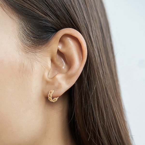 Woman wearing gold chain link huggie hoop earrings