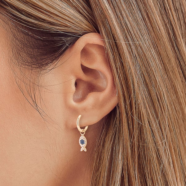 Woman wearing gold ichthys fish huggie hoop earrings