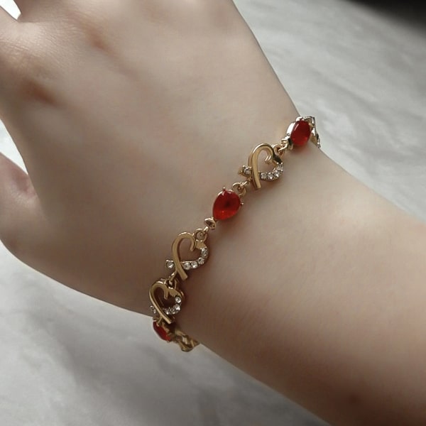 Gold heart chain bracelet with red crystals on a woman's wrist
