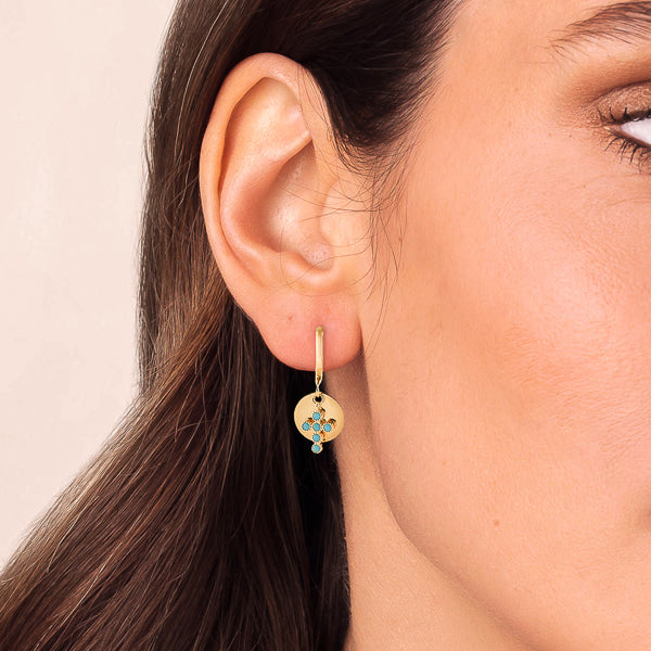 Woman wearing gold and turquoise cross charm hoop earrings