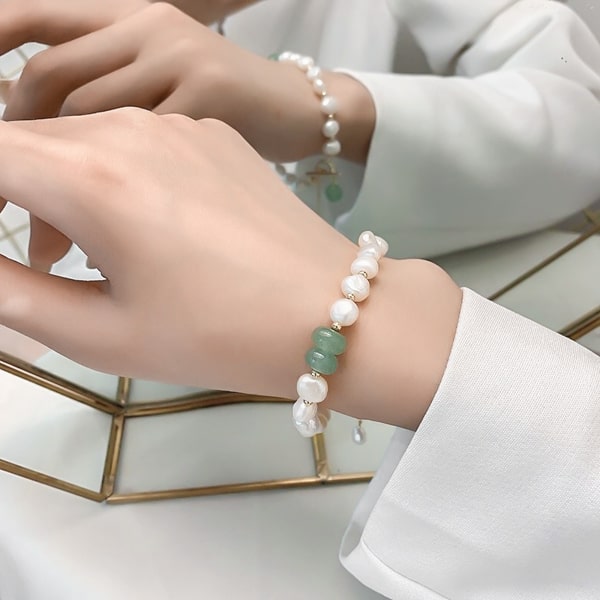 Woman wearing a green jade and white pearl bracelet on her wrist