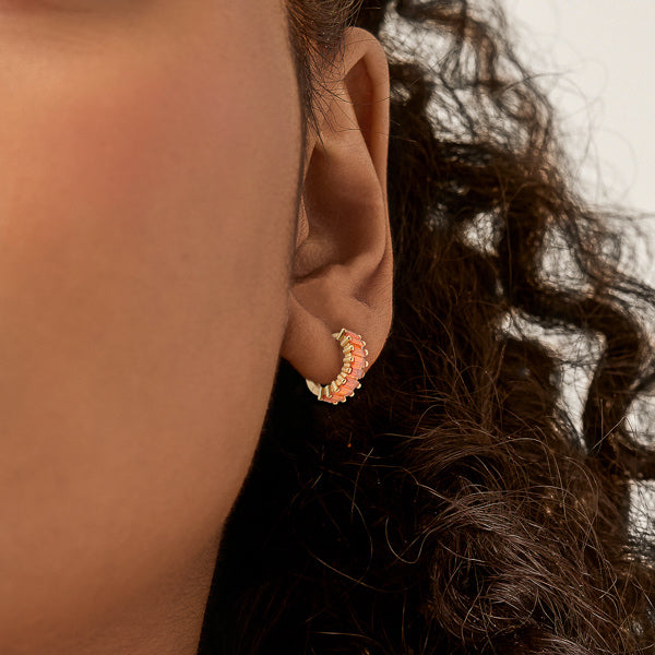 Woman wearing small gold and orange hoop earrings
