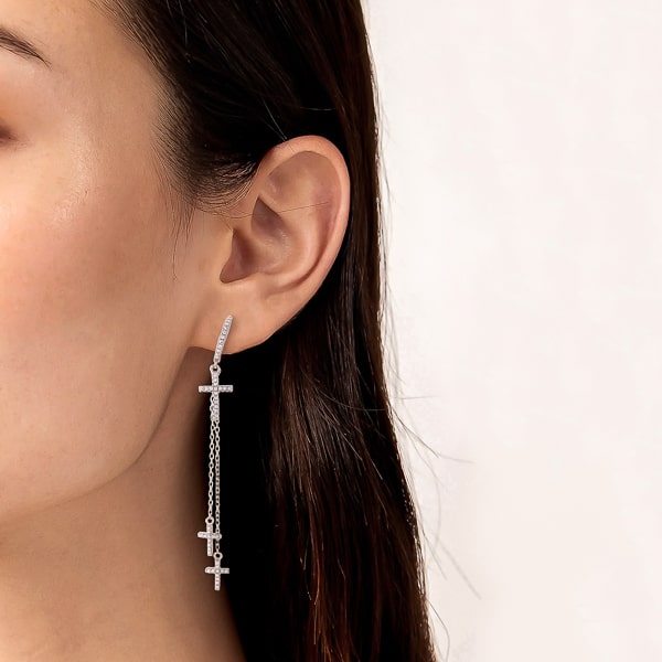 Woman wearing silver crystal cross drop chain hoop earrings