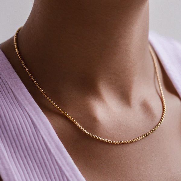 Woman wearing a 2mm gold box chain necklace on her neck