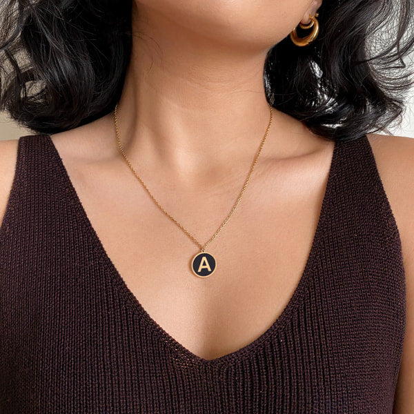 Woman wearing a gold and black round initial coin pendant necklace