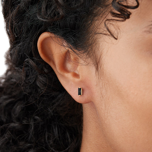Woman wearing gold and black mini baguette stud earrings