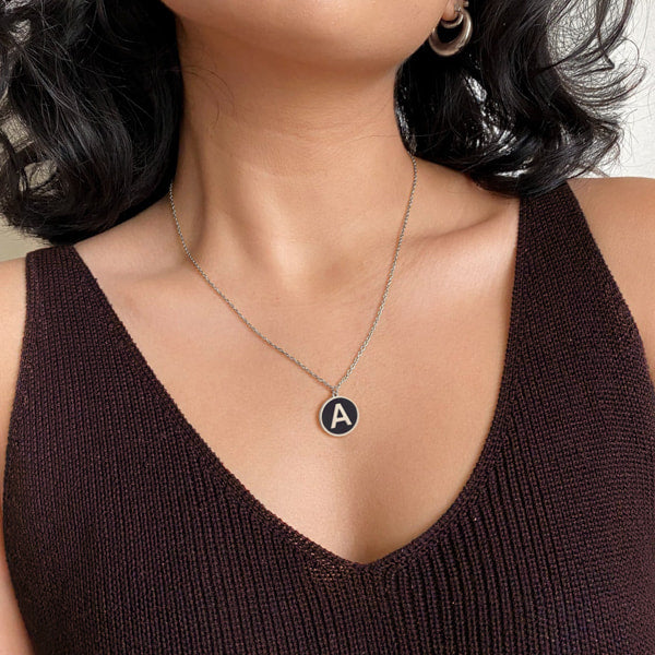 Woman wearing a silver and black round initial coin pendant necklace