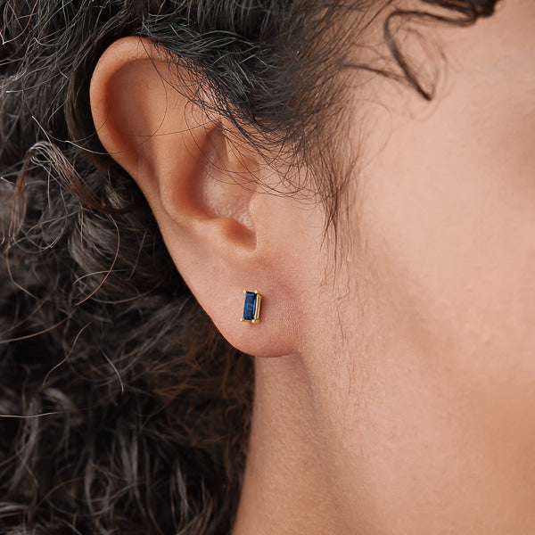 Woman wearing gold and blue mini baguette cubic zirconia stud earrings