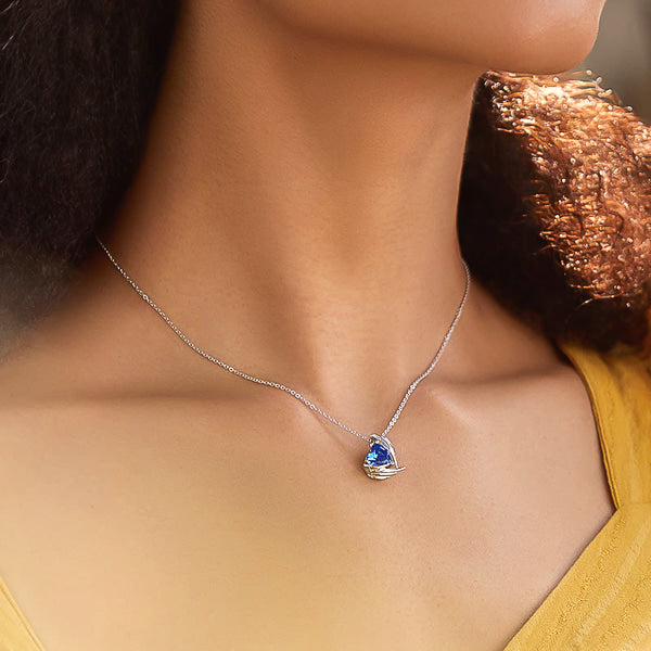 Celtic blue crystal heart and angel wings pendant hanging from a silver chain on a woman's neck