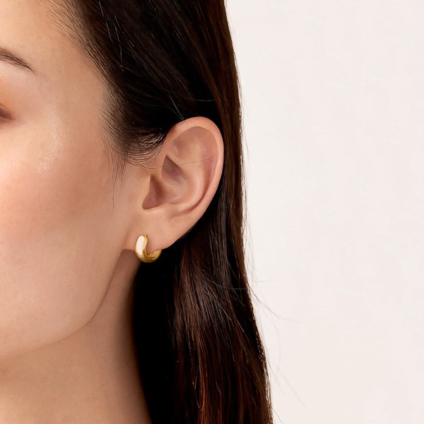 Woman wearing chunky gold huggie hoop earrings