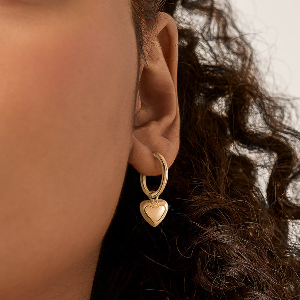 Woman wearing chunky gold dangle heart hoop earrings