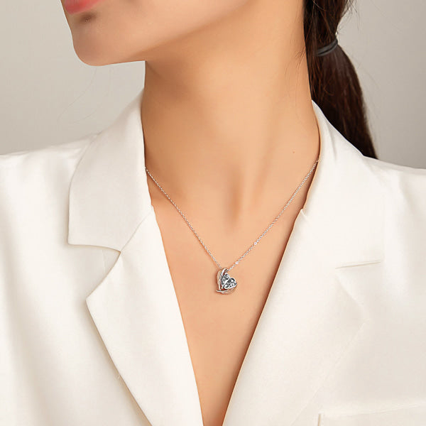Clear white crystal heart and angel wings pendant hanging from a silver chain displayed on a woman's neck
