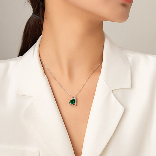 Woman wearing an emerald green crystal heart and angel wings pendant on a silver chain