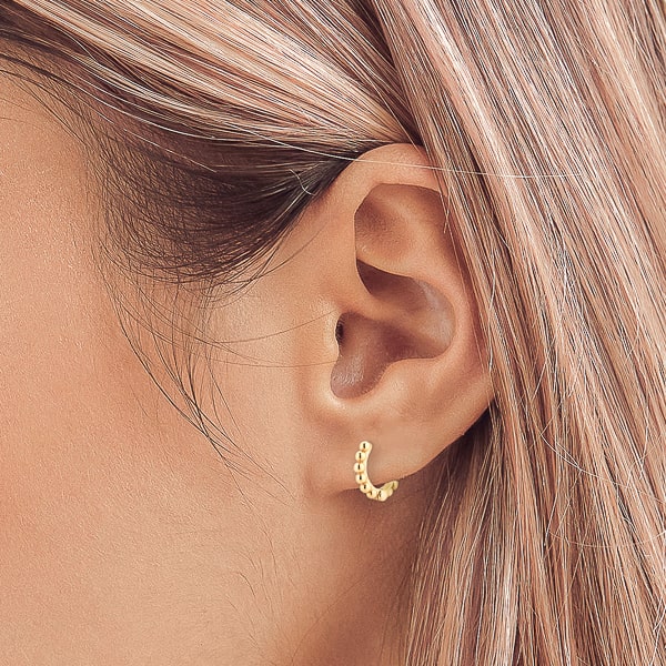 Woman wearing gold bead huggie hoop earrings