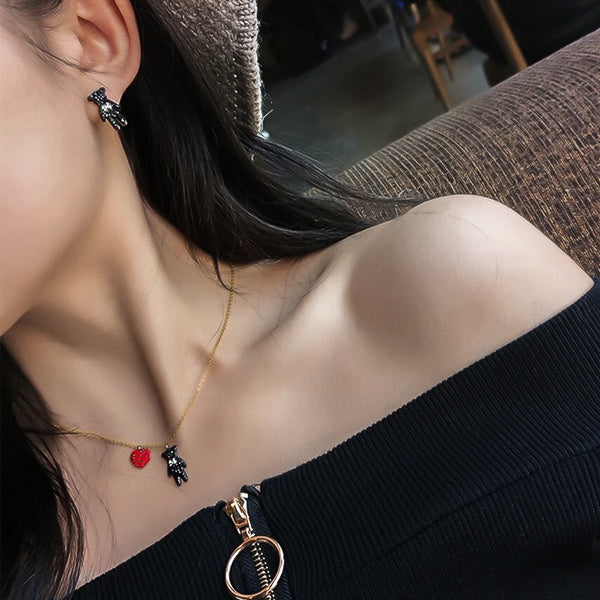 Woman wearing a red crystal heart and black crystal teddy bear pendant on a gold necklace