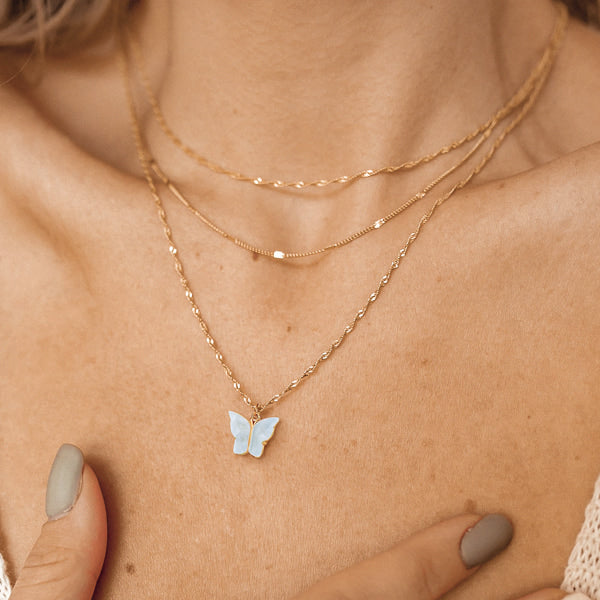 Woman wearing a blue butterfly pendant on a gold necklace