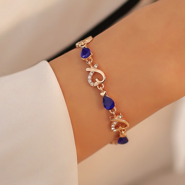 Gold heart chain bracelet with blue crystals on a woman's wrist