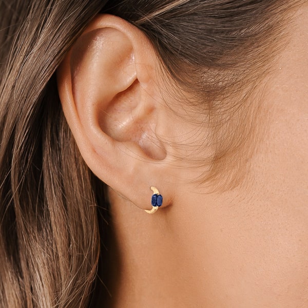 Woman wearing gold blue cushion huggie hoop earrings