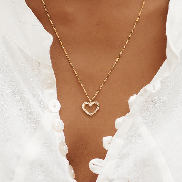 Woman wearing a champagne crystal open heart on a gold necklace