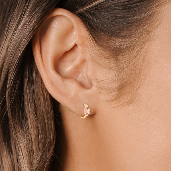 Woman wearing gold champagne cushion huggie hoop earrings