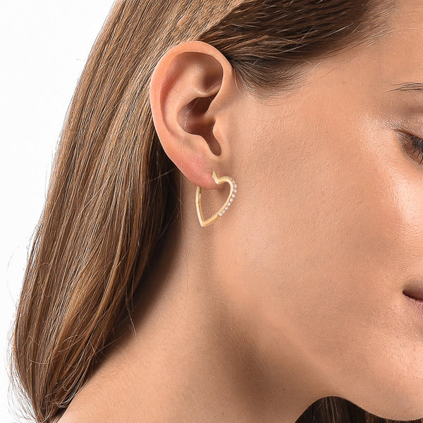 Woman wearing gold crystal heart hoop earrings