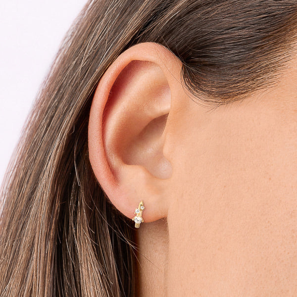 Woman wearing gold crystal mini huggie hoop earrings