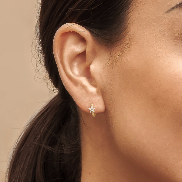 Woman wearing gold crystal star huggie hoop earrings