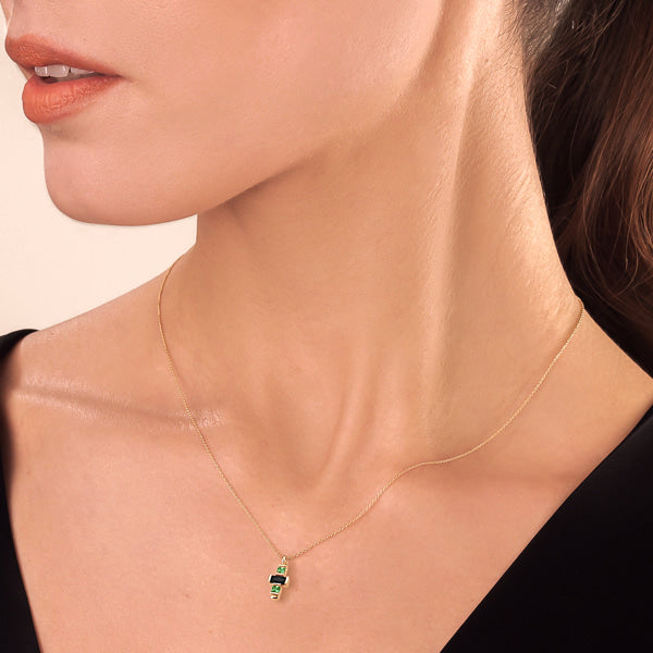 Woman wearing a dainty green & black crystal cross on a gold necklace