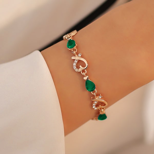 Gold heart chain bracelet with green crystals on a woman's wrist