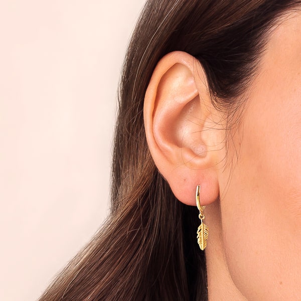 Woman wearing gold mini feather drop hoop earrings