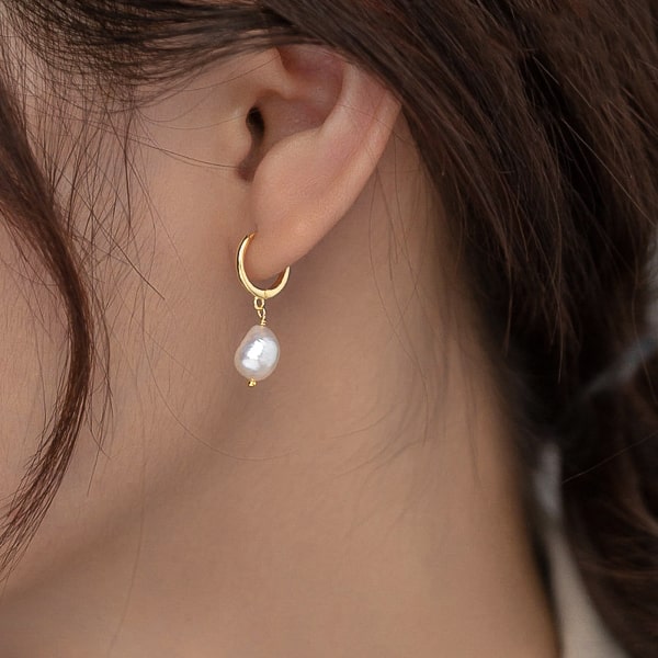 Gold pearl drop hoop earrings on a model