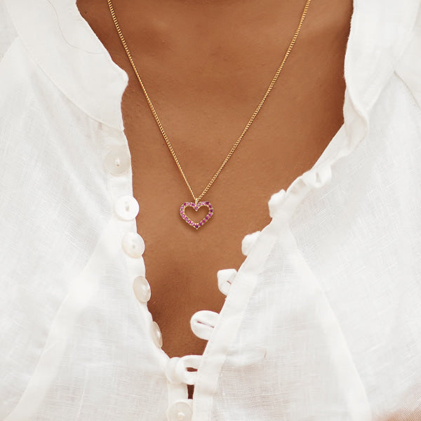Woman wearing a red crystal open heart on a gold necklace