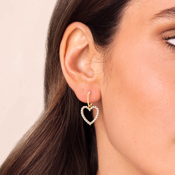 Woman wearing gold crystal heart dangle drop earrings