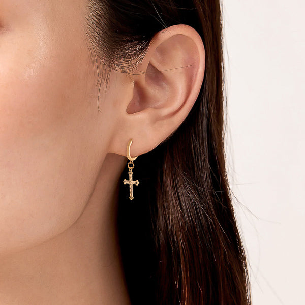 Woman wearing gold vintage cross huggie hoop earrings