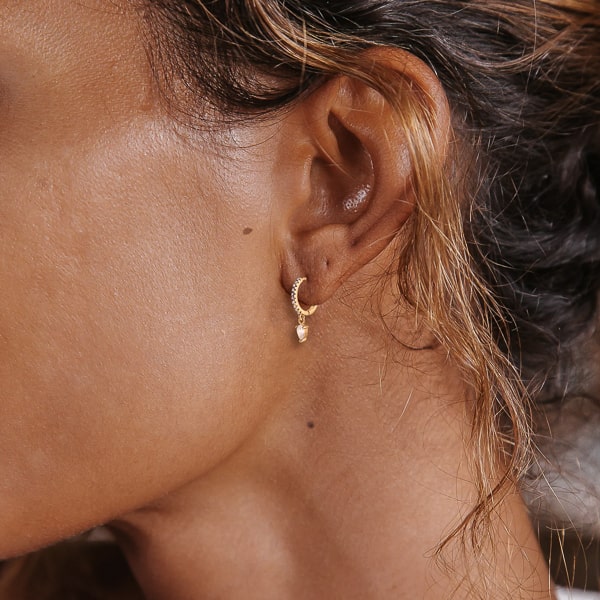 Woman wearing gold white crystal huggie teardrop earrings