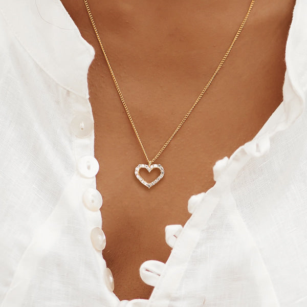 Woman wearing a white crystal open heart on a gold necklace