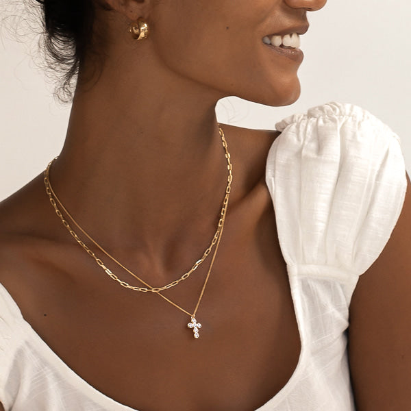 Woman wearing a gold rounded cross necklace with white crystals
