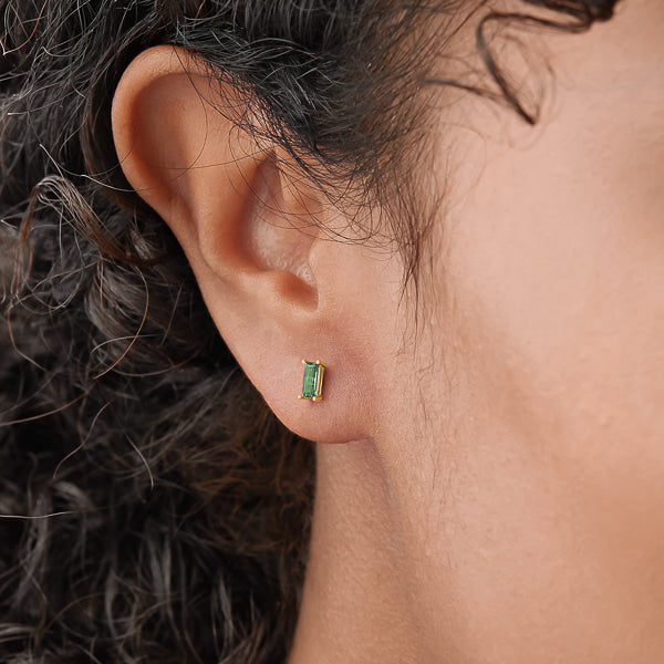 Woman wearing gold and green mini baguette cubic zirconia stud earrings