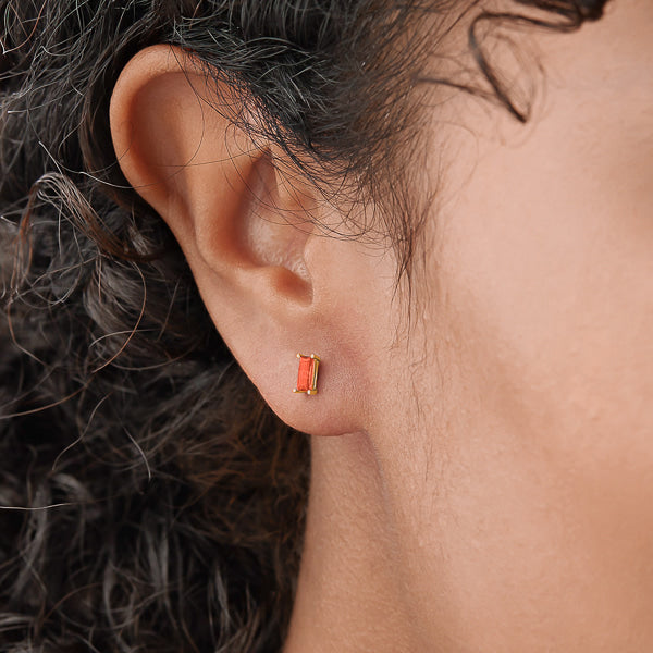 Woman wearing gold and orange red mini baguette cubic zirconia stud earrings