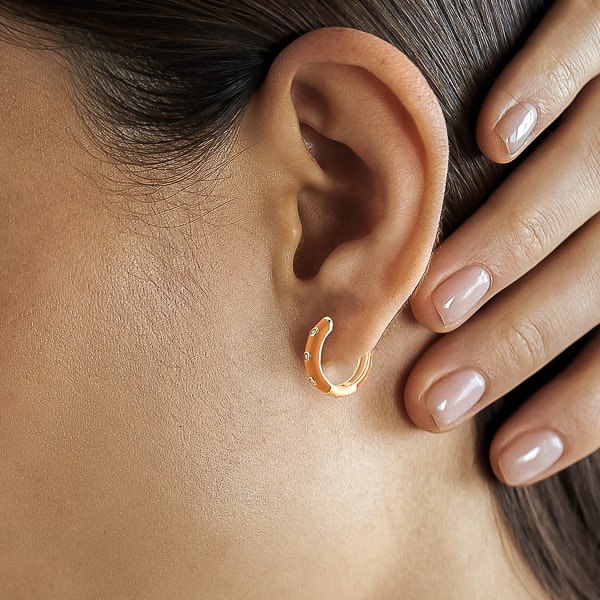 Woman wearing orange enamel mini hoop earrings