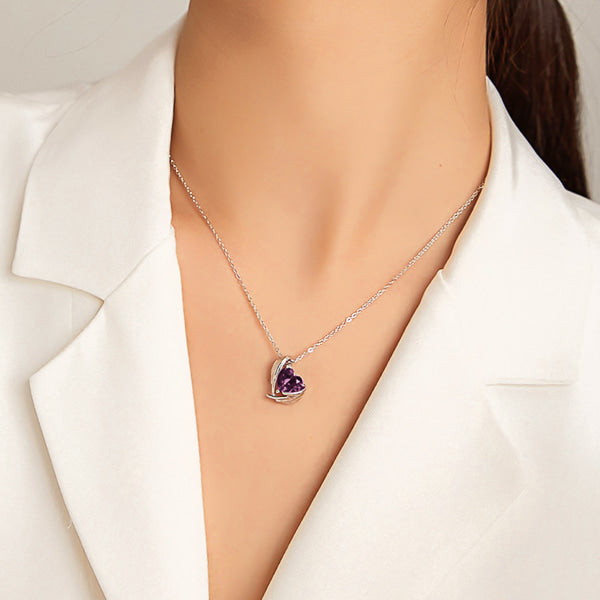 Purple crystal heart and angel wings pendant hanging from a silver necklace on woman's neck