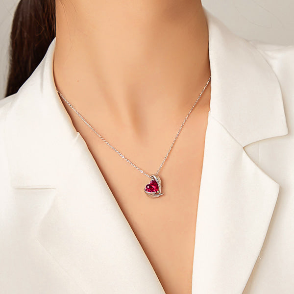 Rose red crystal heart and angel wings pendant hanging from a silver chain on woman's neck