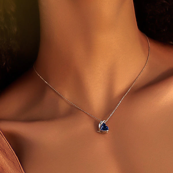 Woman wearing a sapphire blue crystal heart and angel wings pendant on a silver chain
