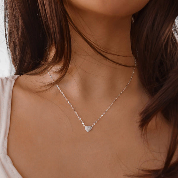 Woman wearing a small silver initial heart necklace