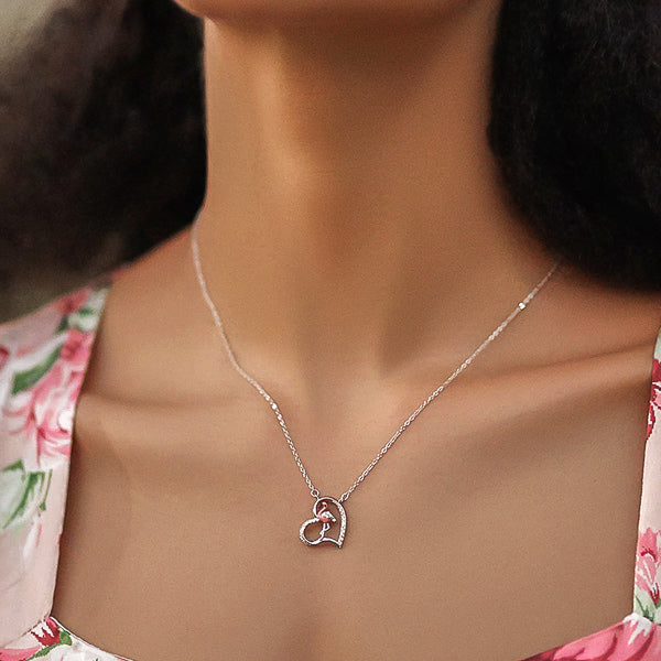 Silver necklace with a heart and a pink flamingo pendant on woman's neck