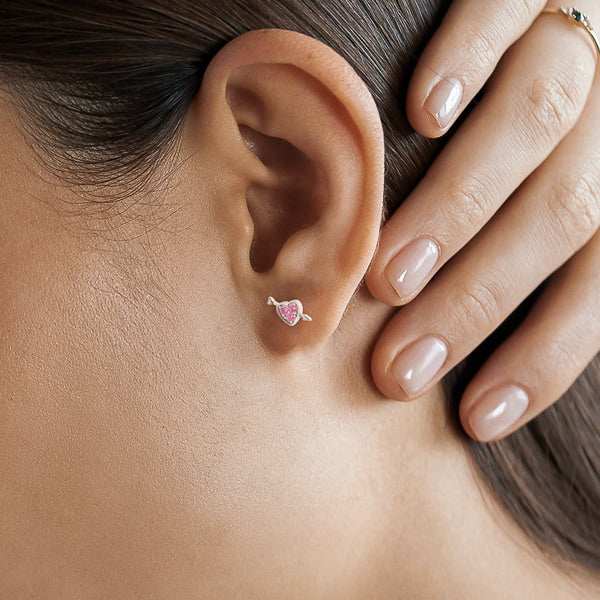 Woman wearing silver heart and arrow stud earrings with pink crystals
