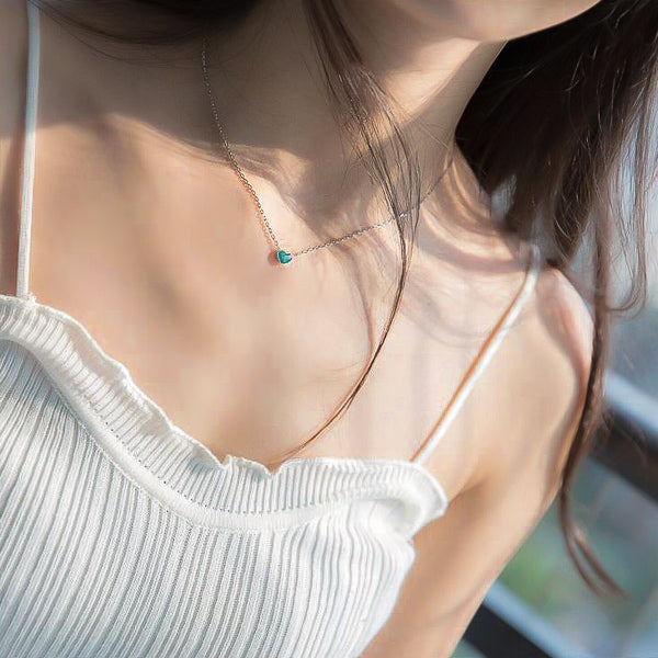 Woman wearing a small green heart on a silver necklace