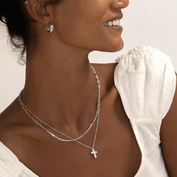 Woman wearing a silver rounded cross necklace with white crystals
